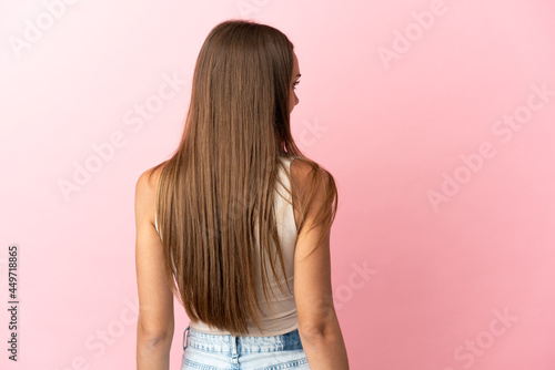 Young woman over isolated pink background in back position and looking side