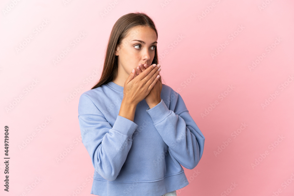 Young woman over isolated pink background covering mouth and looking to the side