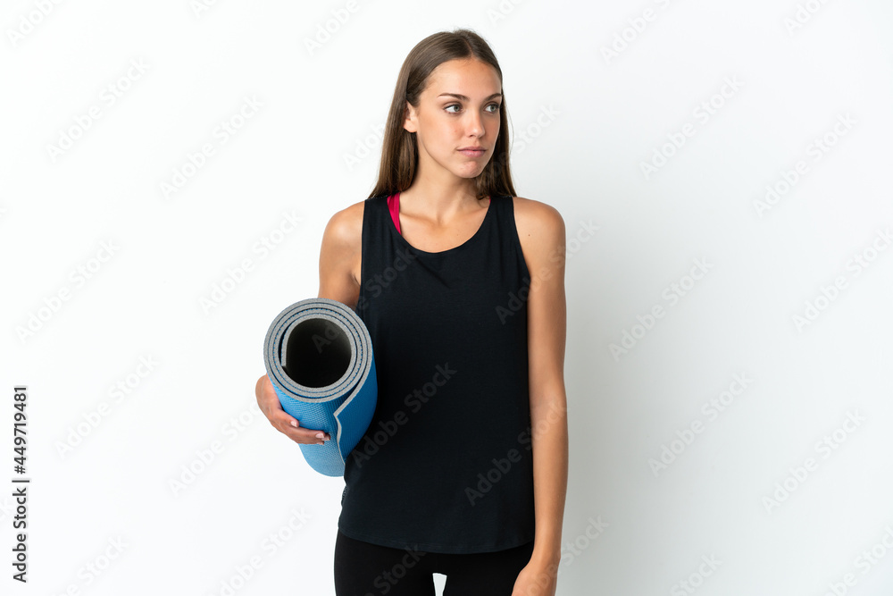 Sport woman going to yoga classes while holding a mat over isolated white background looking to the side Sport woman going to yoga classes while holding a mat over isolated white background looking to the side