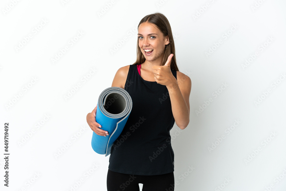 Sport woman going to yoga classes while holding a mat over isolated white background with thumbs up because something good has happened Sport woman going to yoga classes while holding a mat over isolated white background with thumbs up because something good has happened