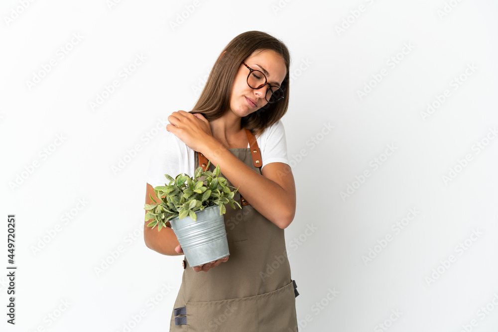 Gardener girl holding a plant over isolated white background suffering from pain in shoulder for having made an effort Gardener girl holding a plant over isolated white background suffering from pain in shoulder for having made an effort