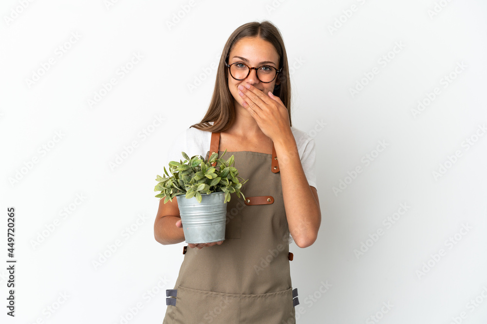 Gardener girl holding a plant over isolated white background happy and smiling covering mouth with hand Gardener girl holding a plant over isolated white background happy and smiling covering mouth with hand