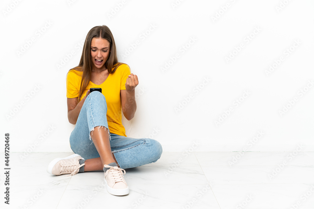 Young girl sitting on the floor surprised and sending a message Young girl sitting on the floor surprised and sending a message