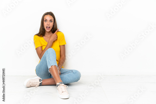 Young girl sitting on the floor surprised and pointing side