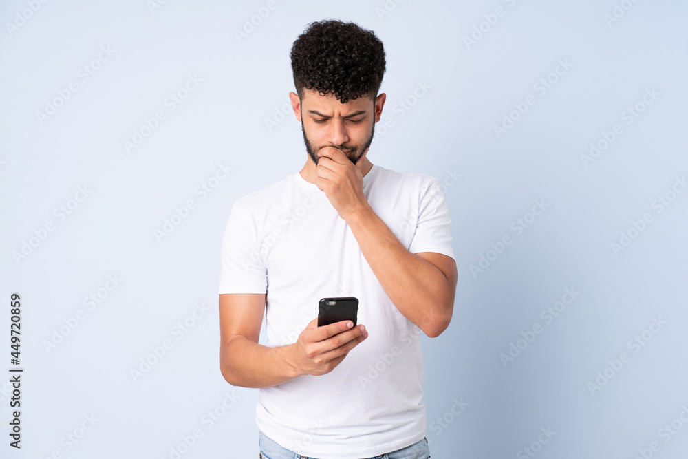 Young Moroccan man isolated on blue background thinking and sending a message Young Moroccan man isolated on blue background thinking and sending a message