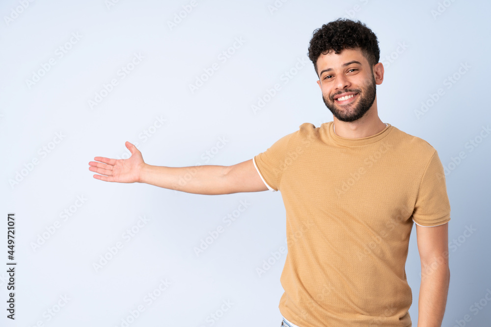 Young Moroccan man isolated on blue background extending hands to the side for inviting to come Young Moroccan man isolated on blue background extending hands to the side for inviting to come