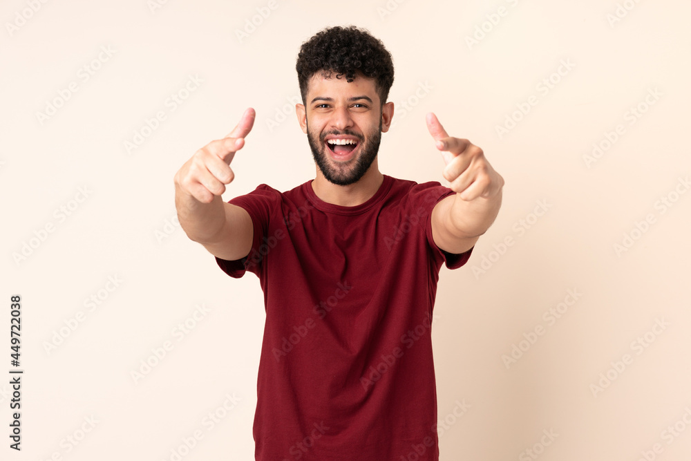 Young Moroccan man isolated on beige background surprised and pointing front Young Moroccan man isolated on beige background surprised and pointing front
