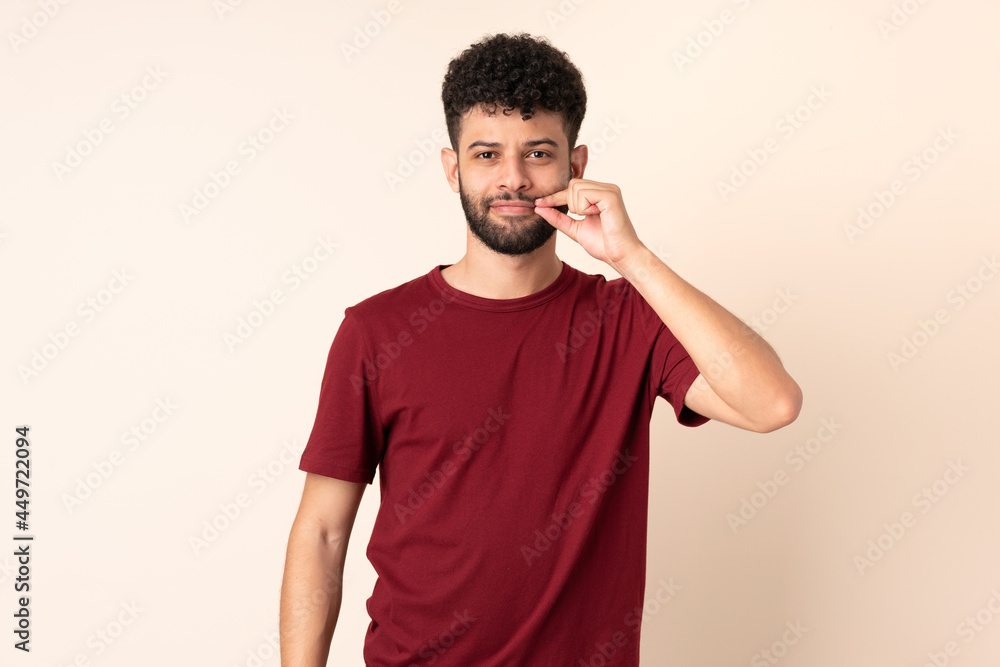 Young Moroccan man isolated on beige background showing a sign of silence gesture Young Moroccan man isolated on beige background showing a sign of silence gesture