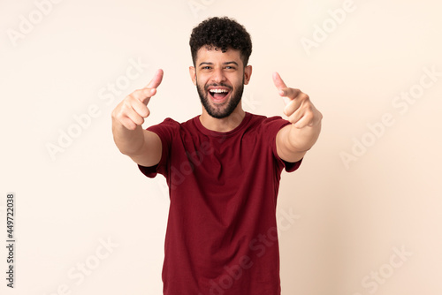 Young Moroccan man isolated on beige background surprised and pointing front © luismolinero