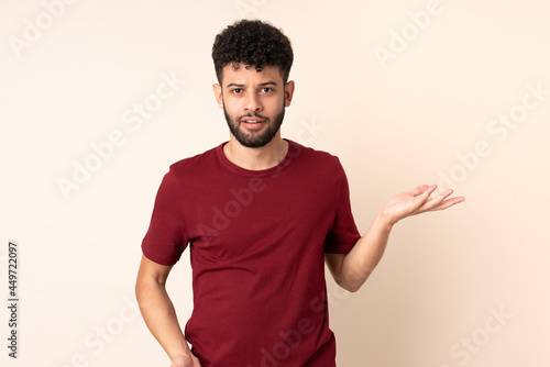 Young Moroccan man isolated on beige background making doubts gesture © luismolinero