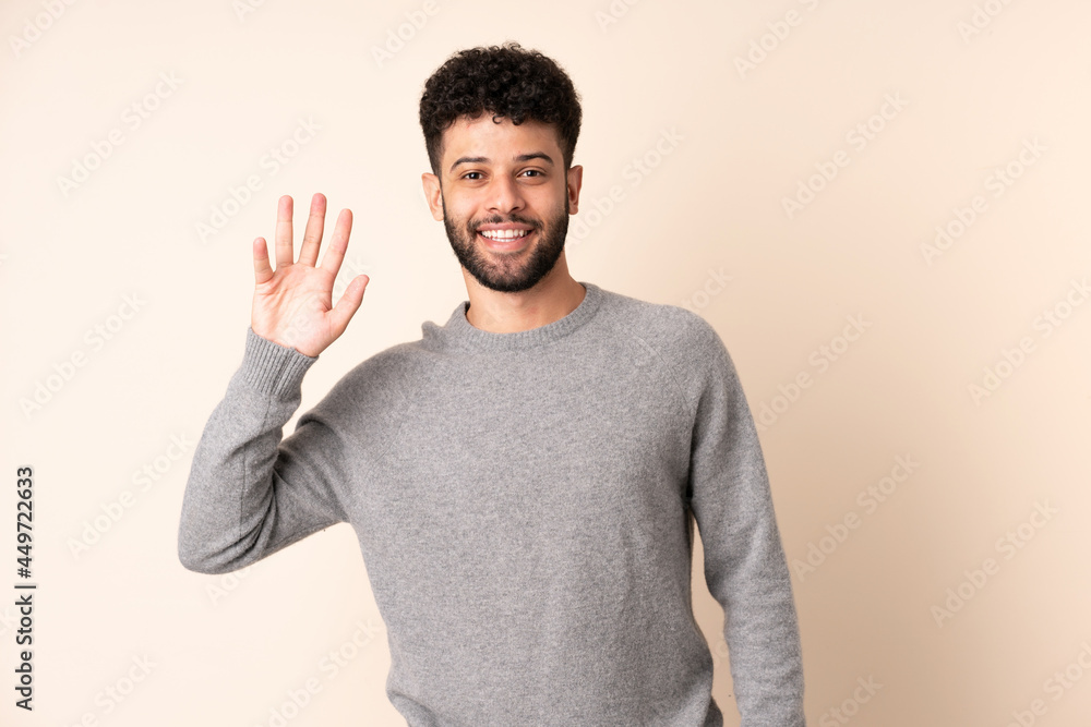 Young Moroccan man isolated on beige background saluting with hand with happy expression Young Moroccan man isolated on beige background saluting with hand with happy expression