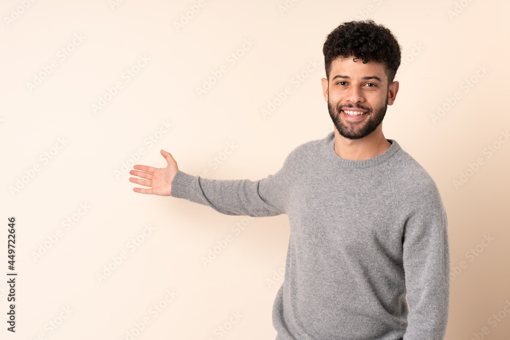 Young Moroccan man isolated on beige background extending hands to the side for inviting to come Young Moroccan man isolated on beige background extending hands to the side for inviting to come