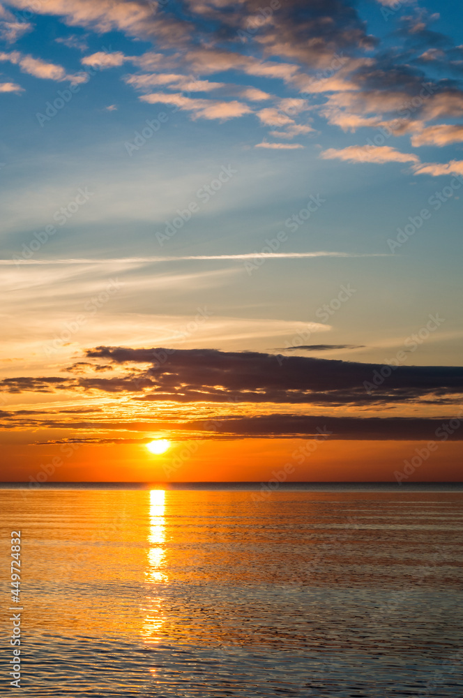 Naklejka premium Sunset over the sea. Reflection of sunlight in the sea waves. Red and yellow sky in the rays of the sunset.