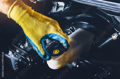 The mechanic is open or close the car's brake fluid reservoir cap to check the brake fluid level