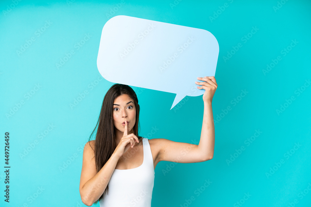 Young Brazilian woman isolated on blue background holding an empty speech bubble and doing silence gesture