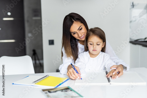 Loving young mother and little preschooler daughter sit at table drawing on paper together. Caring mum or nanny playing with small girl child, paint pictures in notebook, early development concept