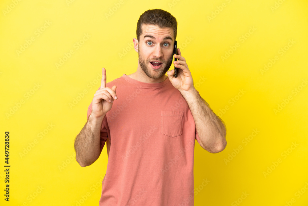 Handsome blonde man using mobile phone over isolated background thinking an idea pointing the finger up