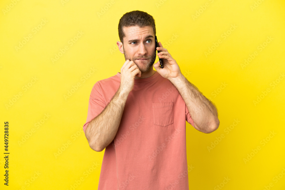 Handsome blonde man using mobile phone over isolated background having doubts and thinking Handsome blonde man using mobile phone over isolated background having doubts and thinking