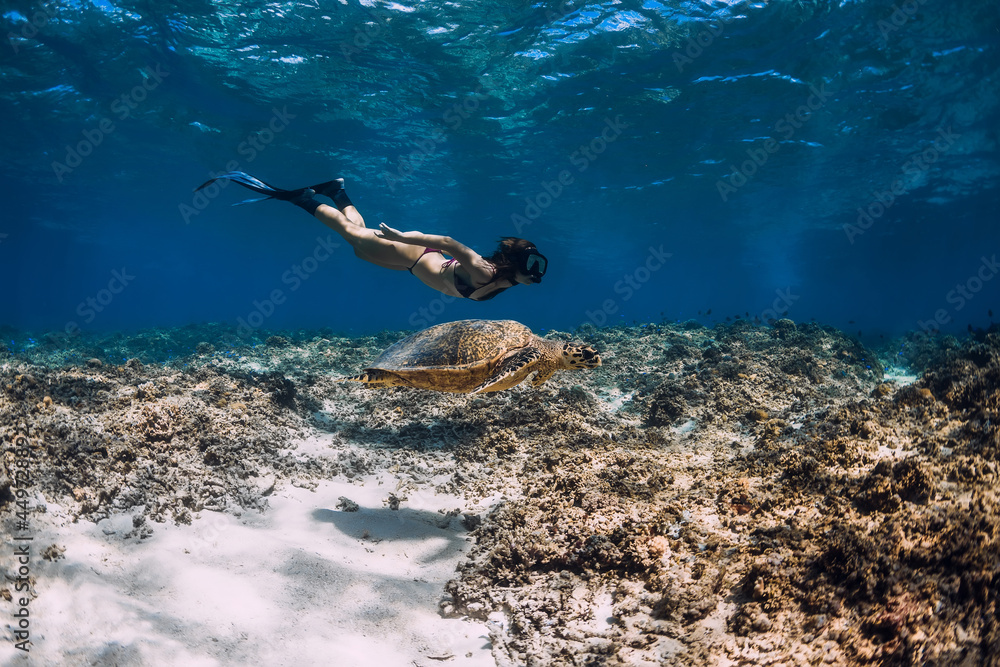 Woman freediver glides underwater ocean with sea turtle.