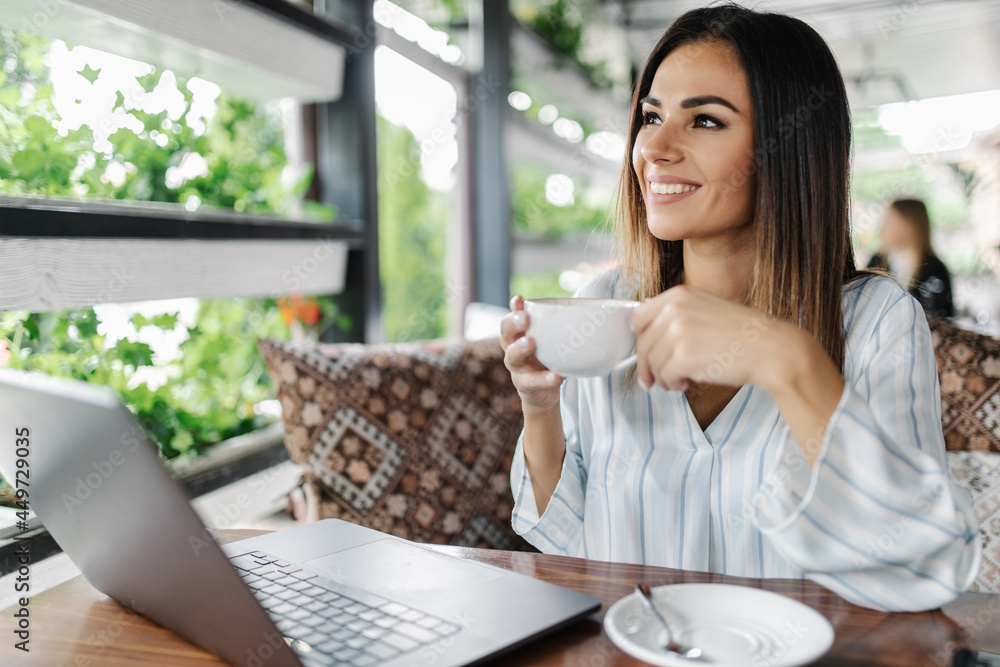 Portrait of gorgeous young woman sitting with open laptop computer in modern coffee shop