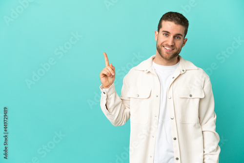 Handsome blonde man over isolated blue background showing and lifting a finger in sign of the best