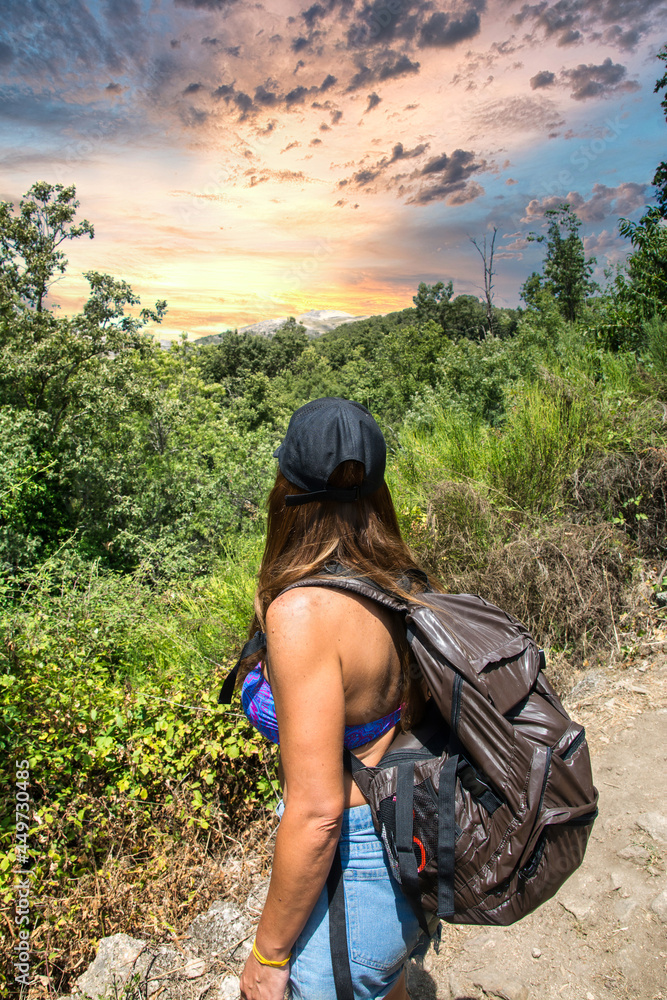 Unrecognizable Hiker Looking At A Dramatic Sky. Young Woman Hiking In A Forest, Carrying A Backpack And Her Back. Rear View Of A Person Who Is In Contact With Nature. Nomadic life concept.