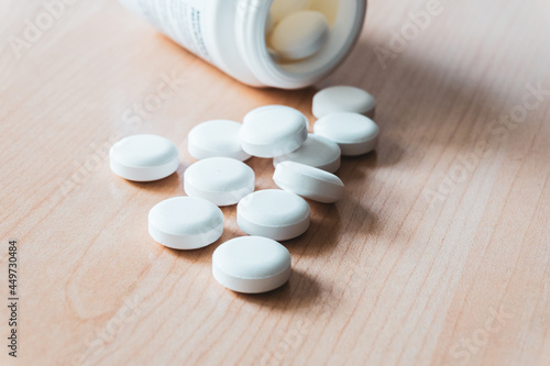 Round medicine pills spread out on a wooden board and the open bottle in the background. 