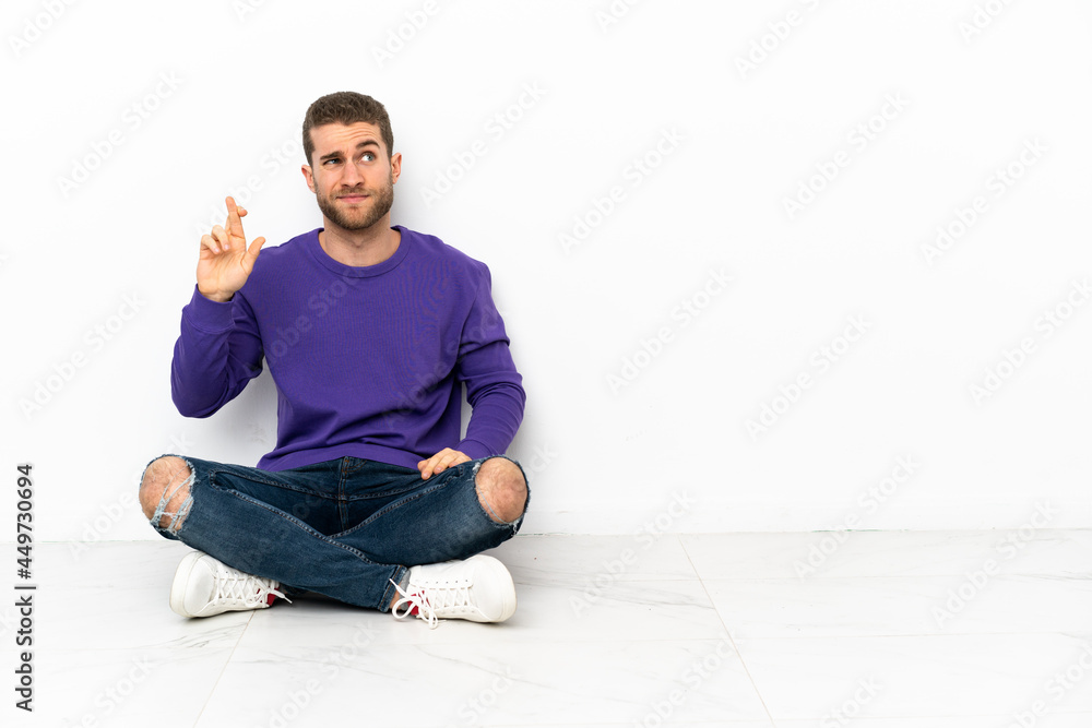 Young man sitting on the floor with fingers crossing and wishing the best Young man sitting on the floor with fingers crossing and wishing the best