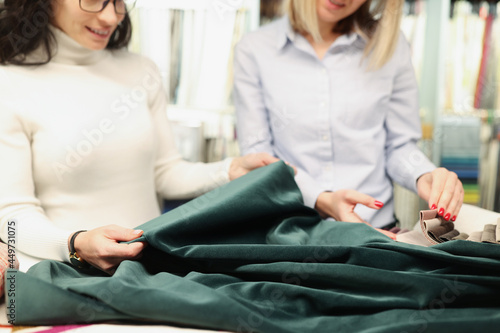 Two women examine fabric of green emerald color photo