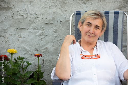 Blonde woman smiling sit looking at the camera with her pink glasses on her neck over a grey background