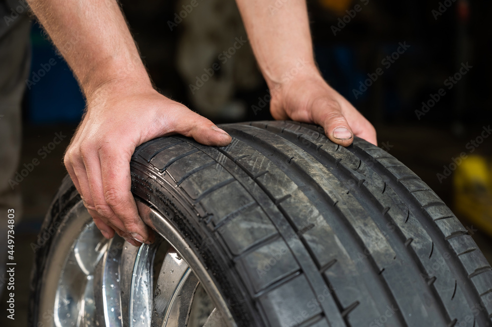 Obraz premium An auto mechanic holds a wheel of a car. Change of car tires according to the season