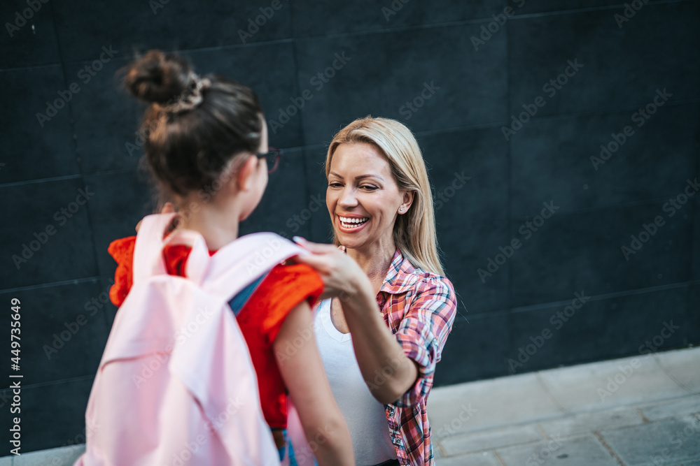 Mom saying goodbye to her daughter before going to school. Back to school and education concept.