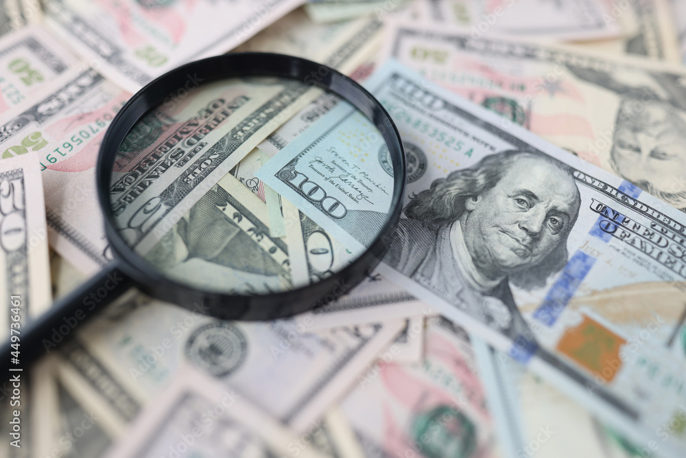 One hundred dollar bills and magnifying glass lie on table closeup One hundred dollar bills and magnifying glass lie on table closeup