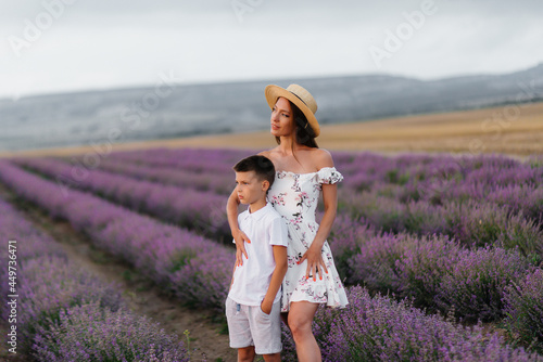 Fototapeta Naklejka Na Ścianę i Meble -  A young beautiful woman with her young son is walking through a beautiful field of lavender and enjoying the fragrance of flowers. Rest and beautiful nature. Unity with nature and harmony.