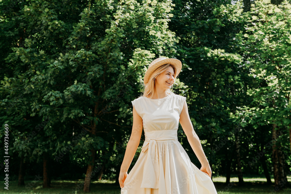 Beautiful young woman in a straw hat and white dress in a green park or forest on a summer day