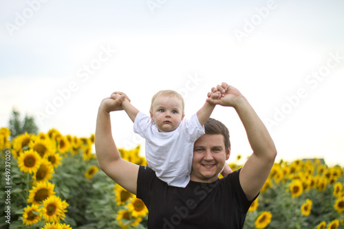 brunette male young dad with cute child blonde son on a field of sunflowers.