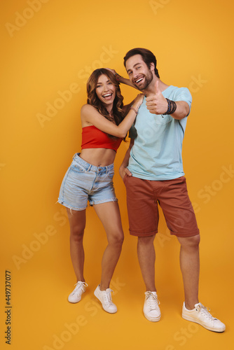 Full length of beautiful young couple smiling while standing against yellow background © gstockstudio