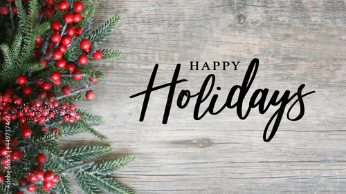 Happy Holidays Script Text with Holiday Evergreen Branches and Red Berries on Side Over Rustic Wood Background