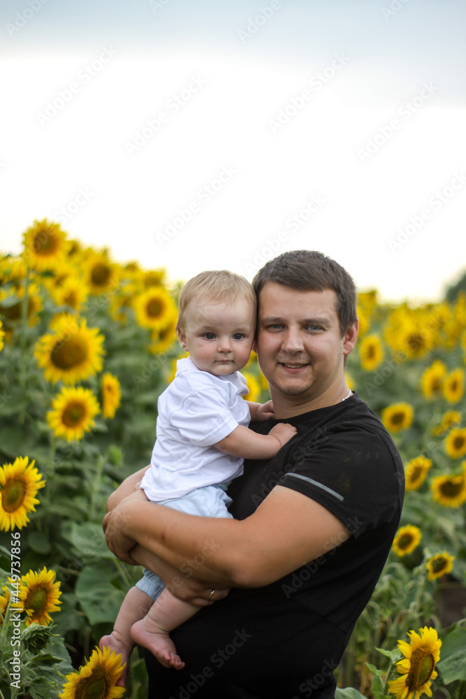 brunette male young dad with cute child blonde son on a field of sunflowers. brunette male young dad with cute child blonde son on a field of sunflowers.