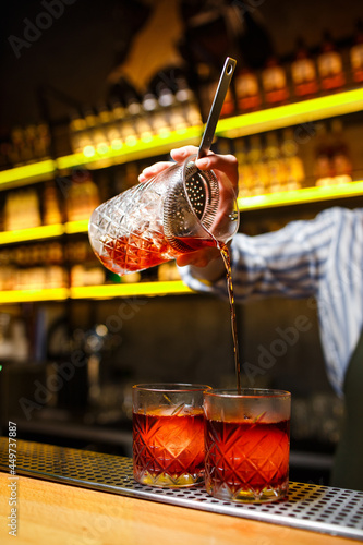 bartender preparing a Negroni cocktail on a dark background of a bar with yellow backlight