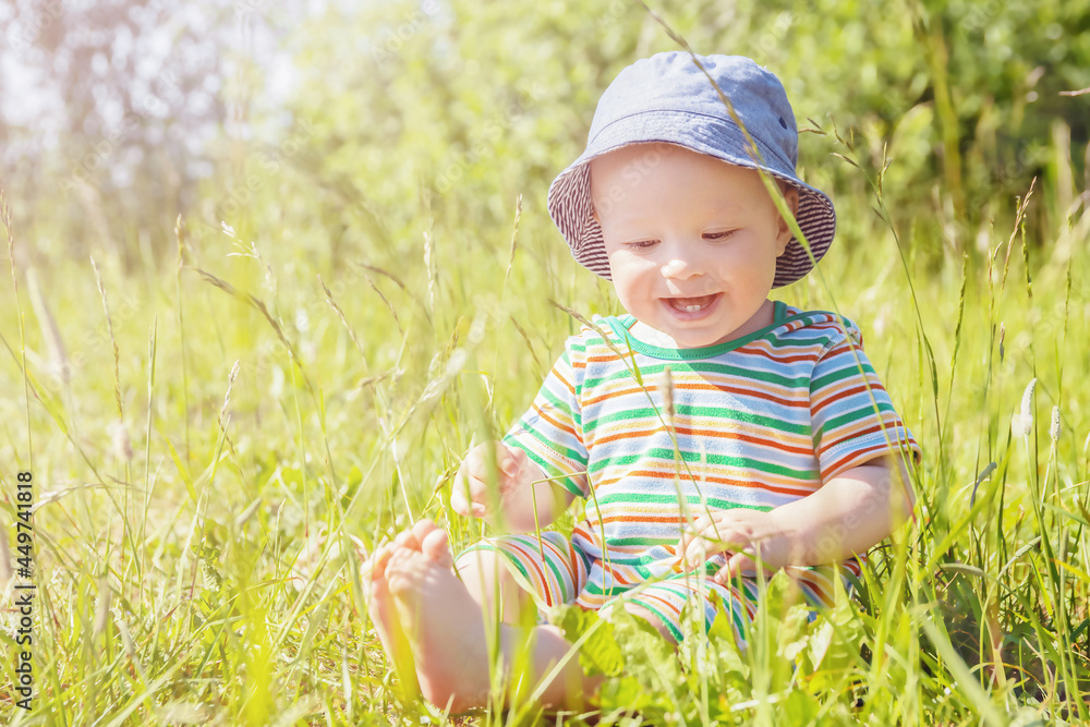 cheerful charming baby in panama hat is sitting on meadow on sunny summer day, summer time, children's day cheerful charming baby in panama hat is sitting on meadow on sunny summer day, summer time, children's day