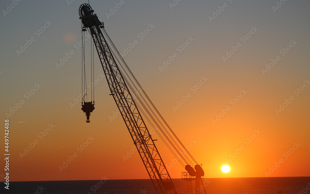 Sunset with a construction crane on the sea