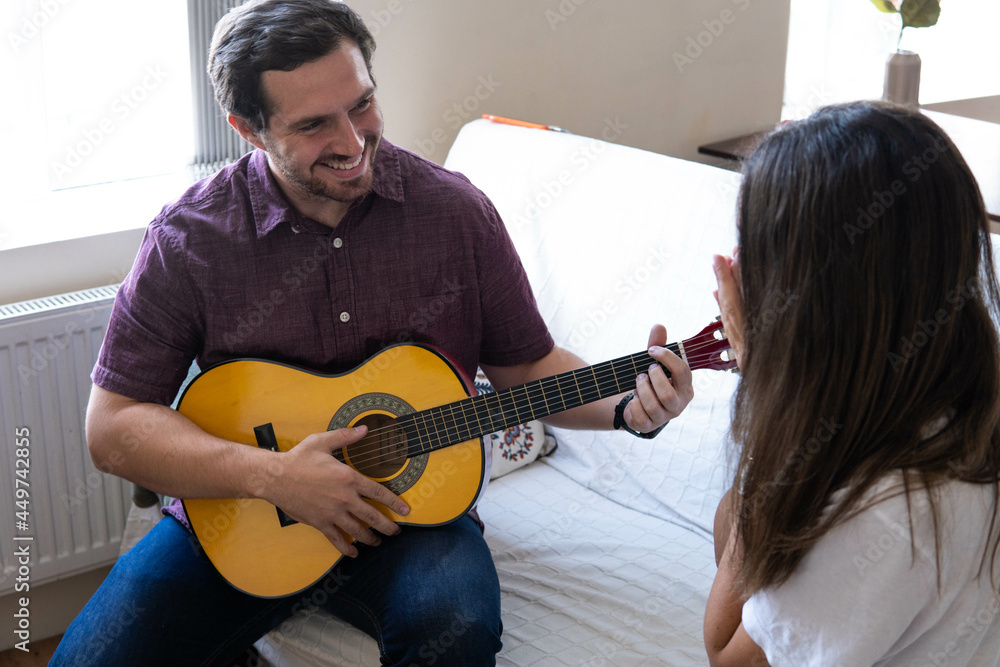 Young and attractive guy playing a romantic song in the guitar to his girlfriend while enjoying a day at home. Woman is surprised and happy listening to his song.