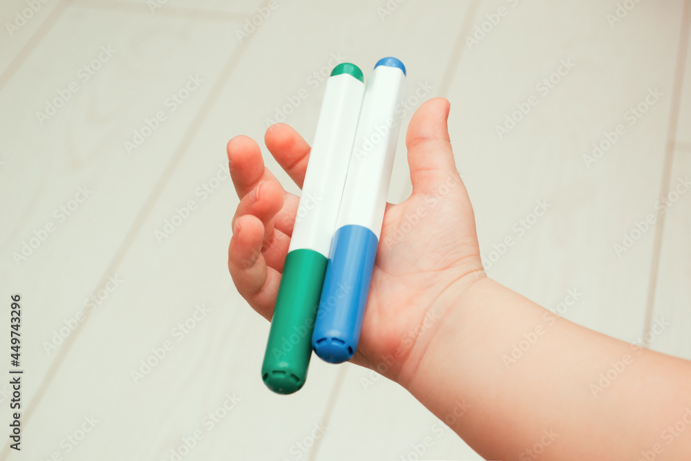 A child's hand holds two felt-tip pens. A child's hand holds two felt-tip pens.