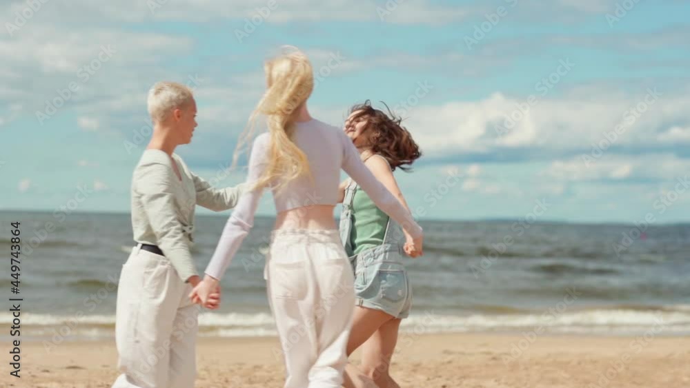 Slow motion panning shot of three happy girlfriends dancing in circle holding hands on beach. Loving women enjoying vacation, freedom and friendship on sea coast Slow motion panning shot of three happy girlfriends dancing in circle holding hands on beach. Loving women enjoying vacation, freedom and friendship on sea coast