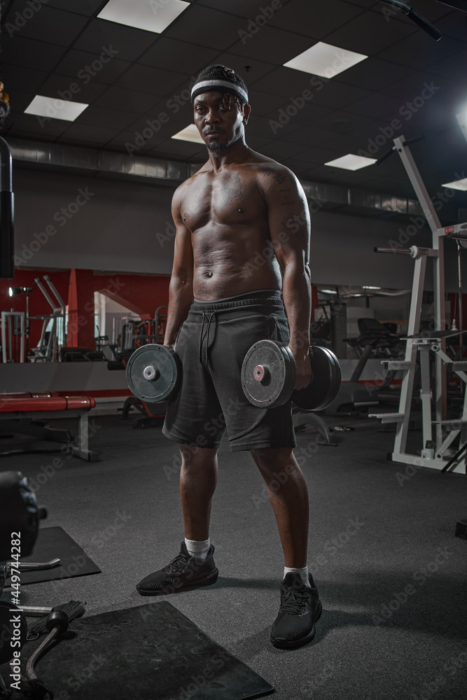 Muscular african american man exercising with weights. Power athletic guy on training pumping up muscles with dumbbells Muscular african american man exercising with weights. Power athletic guy on training pumping up muscles with dumbbells