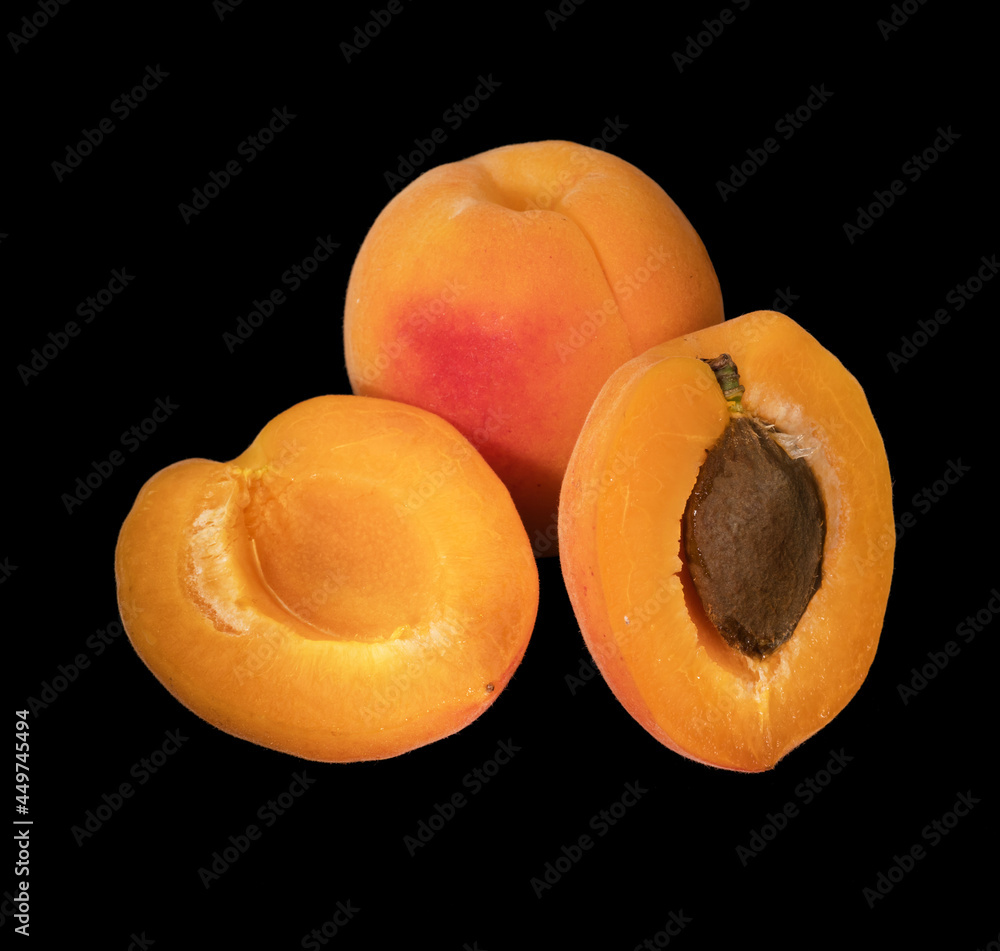 Ripe apricot fruits whole and in pieces on a black background isolated