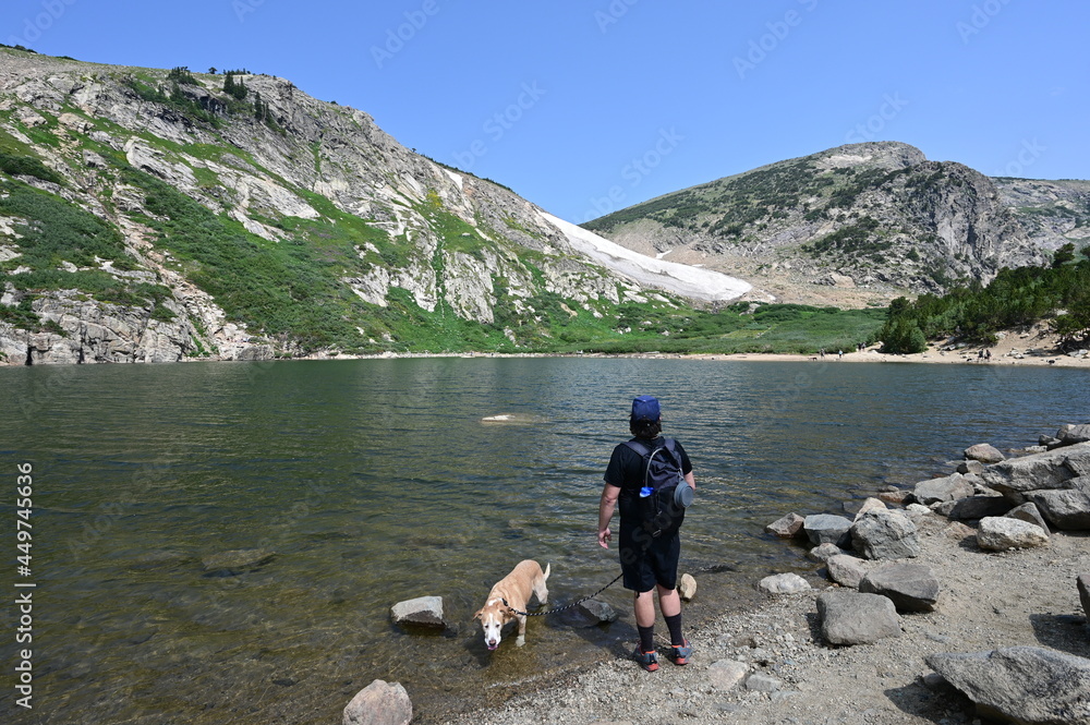 Man and his dog by Saint Mary's Lake under St Mary's Glacier in Arapaho National Forest, Colorado on sunny summer morning.