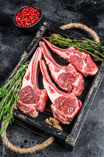 Raw lamb meat chops steaks in a wooden tray. Black background. Top view