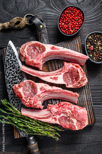 Lamb chops raw meat on bone with salt, pepper and herbs. Black wooden background. Top view